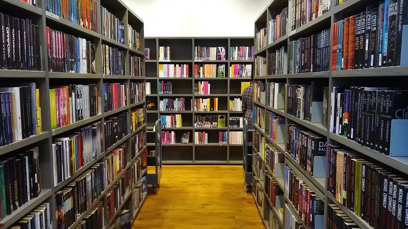 A public library aisle lined with tall bookshelves full of books.