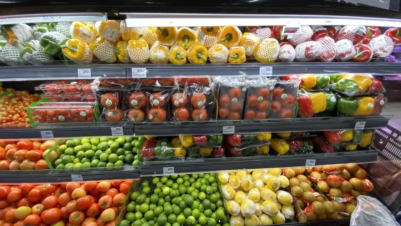 A grocery store produce case stacked with tomatoes, limes, peppers and lemons.