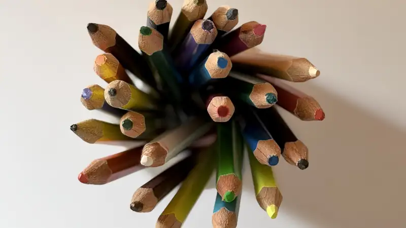 Sharpened colored pencils bundled together, seen from above on a white surface.