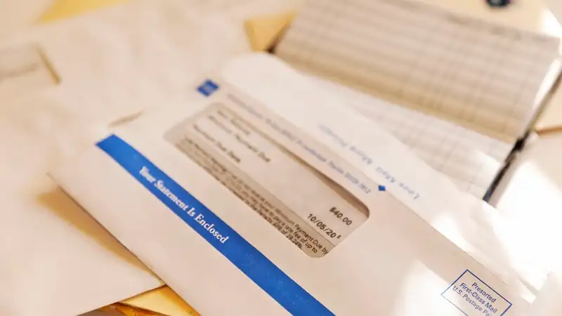 Window envelopes, a statement and a check register piled together on a table.