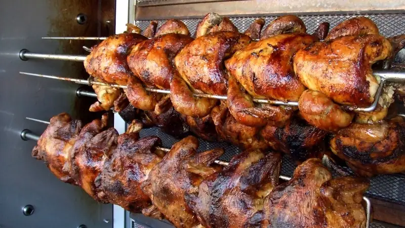 Rows of whole rotisserie chickens roasting on spits, browned and glistening.