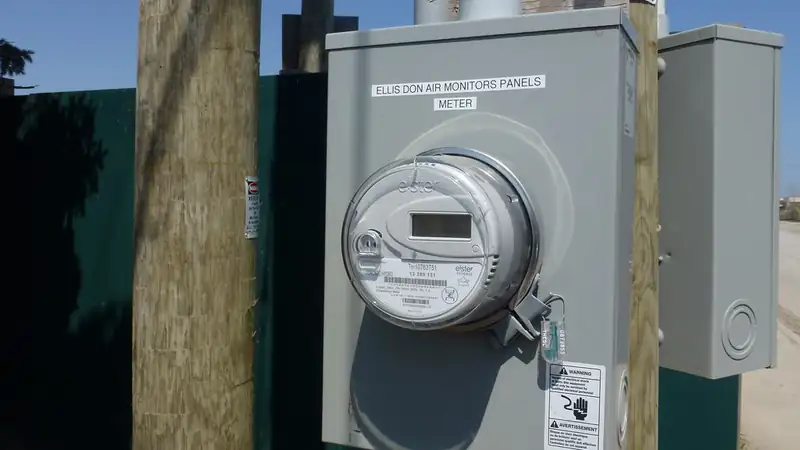 A digital electric meter in a gray box mounted on a wooden utility pole.
