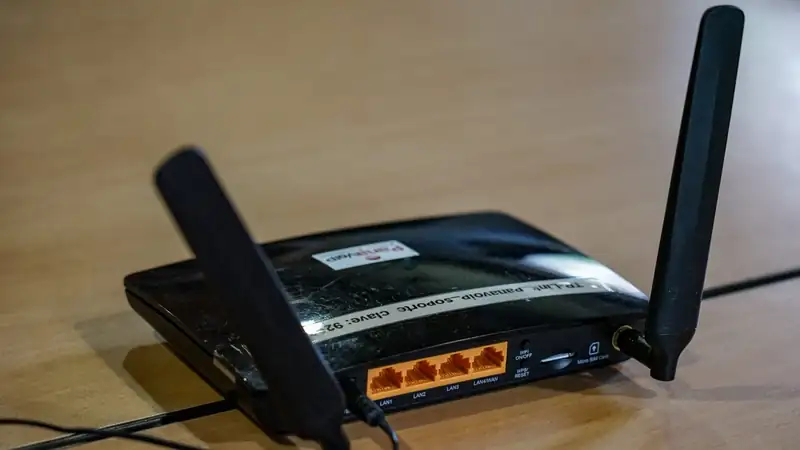 A black Wi-Fi router with two antennas and yellow ethernet ports on a wooden desk.