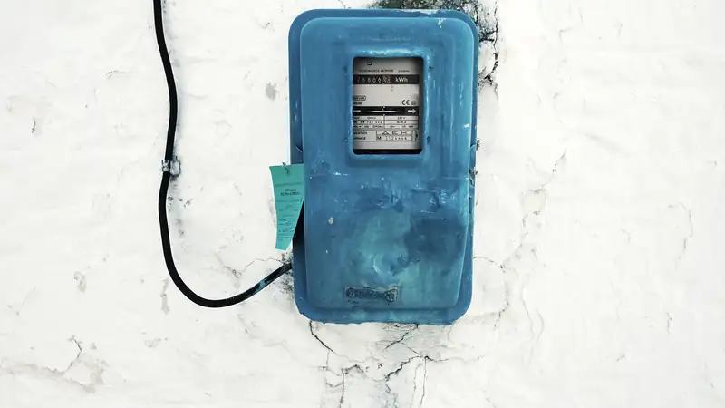 A blue electricity meter box with a black cable on a white plaster wall.